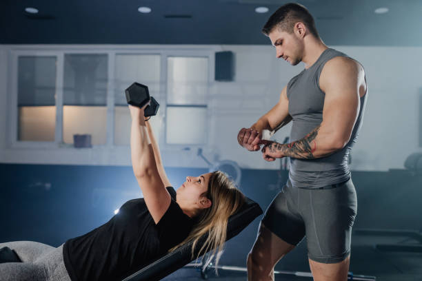 istock Coach keeping track while woman exercise with dumbbells at gym 1392978430