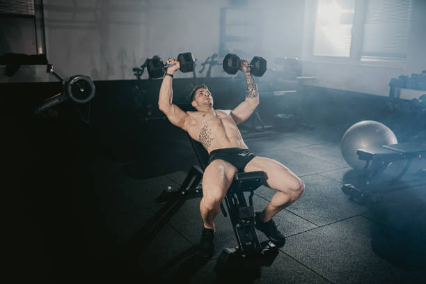 istock Muscular athlete doing strength training with dumbbells on bench at gym 1392979714