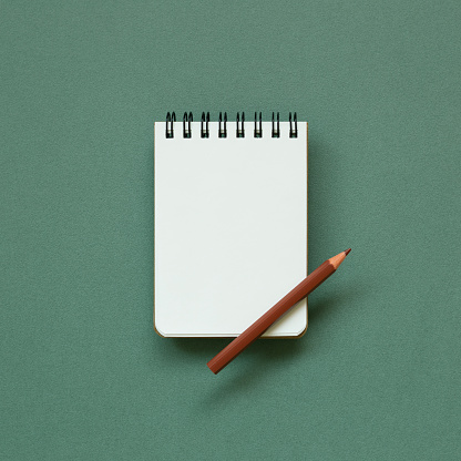 Empty memo note pad with brown pencil on green background. top view, copy space