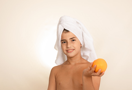 Boy with towel on his head holds an orange and looks at the camera. Spa, health and beauty day