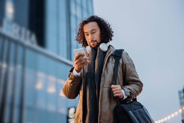 istock Businessman with black curls using his smartphone in front of an office Building 1392981151