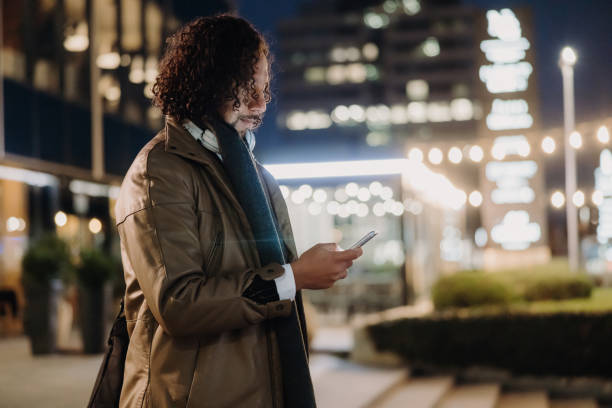 istock Businessman with curly hair replying a message on his smartphone after work, walking down a staircase in the evening 1392982078