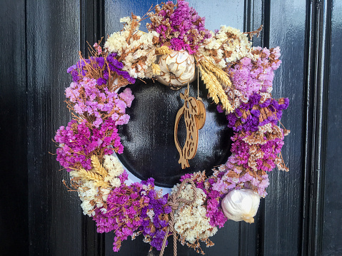Close-up of a decorative wreath with bright lilac flowers and spikelets of wheat hanging on the door of a house.