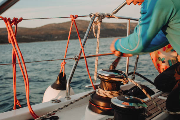 istock Sailor with blue pullover turns a crank Winde to retract the sail, blurred motion, sitting on boat deck of a sailboat on the sea, looking down 1392983526