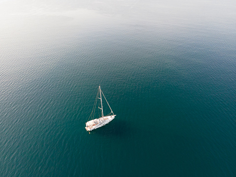 White large Sailboat on calm sea, retraced sail, drone shot view from high angle during daylight