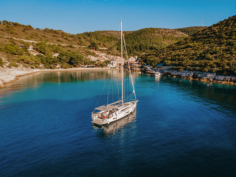 View from above, stunning aerial view of a luxury sailboat floating on a beautiful turquoise clear sea that bathes the green and rocky coasts of Sardinia. Emerald Coast (Sardinia) Italy.