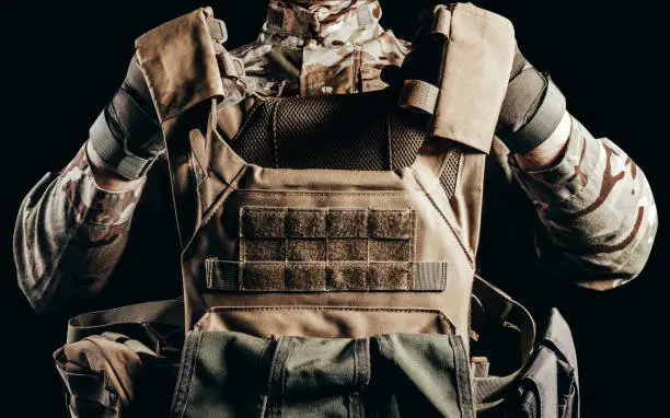 Photo of Soldier in gloves holding miltary armor vest.