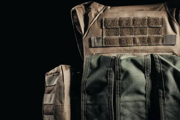 Photo of tactical military soldier armored vest with pouches close-up view on dark background.