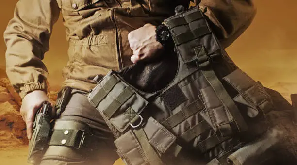 Soldier in military outfit with bulletproof vest. Photo of a soldier in military outfit holding a gun and bulletproof vest on orange desert background.