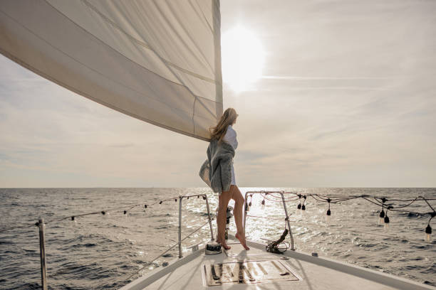 istock Women with grey pullover and long hair looking at the sky in the distance while standing on front boat deck of a sailboat on the sea 1392988025