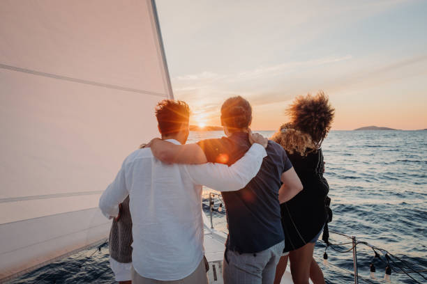 istock Friends hugging each other while standing on front boat deck of a sailboat in the evening, looking at a beautiful sunset on the horizon 1392988376