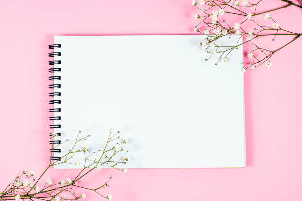 istock Whate blank notebook page with copy space for text with little flowers on pastel pink background top view. Empty wedding paper mockup, romantic Valentine letter template 1392988560