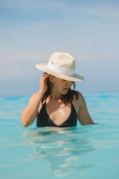 woman in white hat and black swimsuit in blue sea water woman in white hat and black swimsuit in blue sea water summer vacation egremni beach lefkada island greece stock pictures, royalty-free photos & images