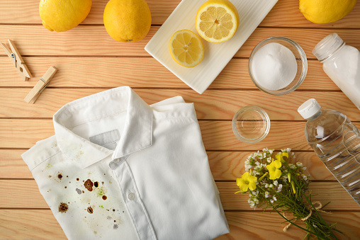 Comparison and concept of cleaning and washing clothes with natural and environmentally friendly products with half dirty and half clean shirt on wooden table with sustainable products around.