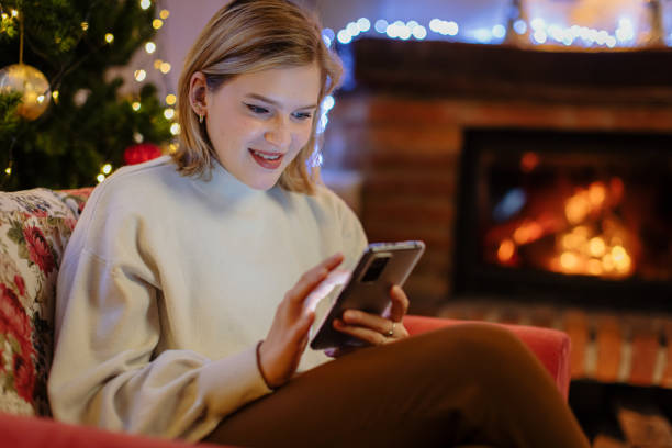 istock Smiling woman using cellphone while relaxing on armchair at home in Christmas 1392992196