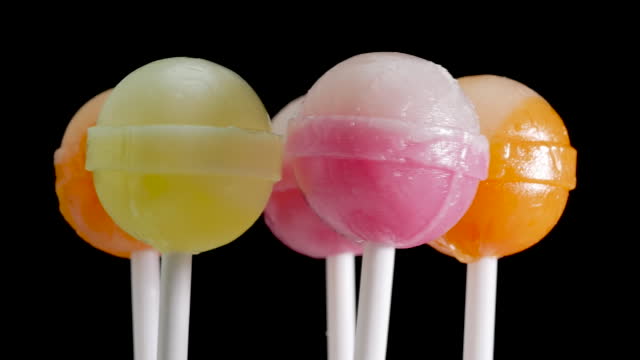 Children's sweets lollipops. A lot of colorful candies are spinning on a black background. Sweet candies on a white stick