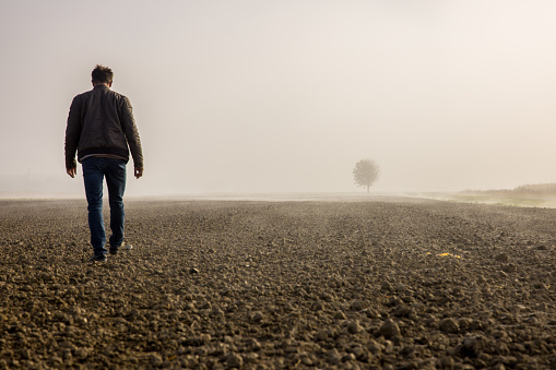 Male farmer walking on plowed agricultural field covered with fog