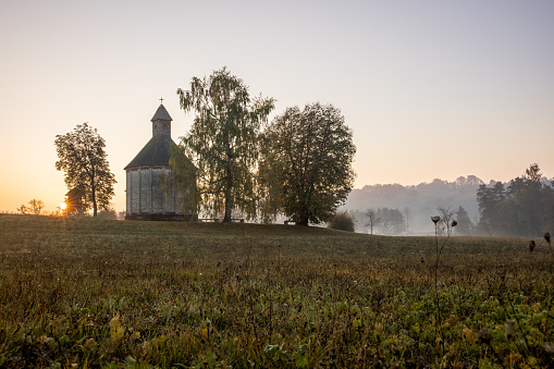 Small beautiful chapel on hill with foggy rural landscape against sky during sunrise