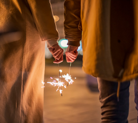 Midsection of couple holding sparklers while enjoying Christmas night together in city