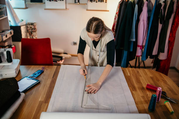 istock Young female tailor making drawings on paper for new cloth over table in workshop 1392996405