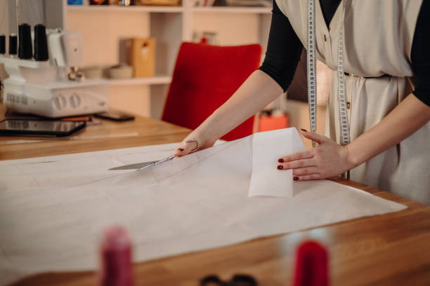 istock Young female tailor cutting paper with scissors on table in workshop 1392997568