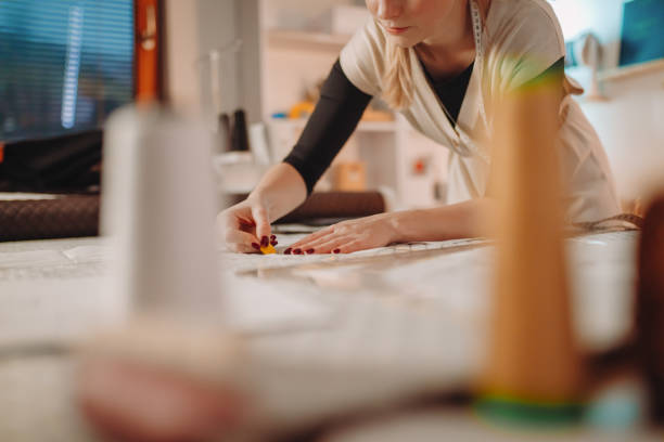 istock Young female tailor drawing pattern on fabric with chalk over table in workshop 1392997685