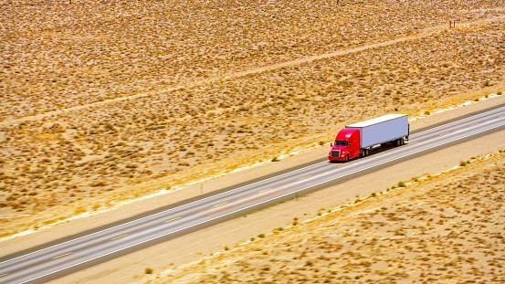 Aerial view of highway passing through desert landscape and red truck driving along it in Nevada, California, USA.