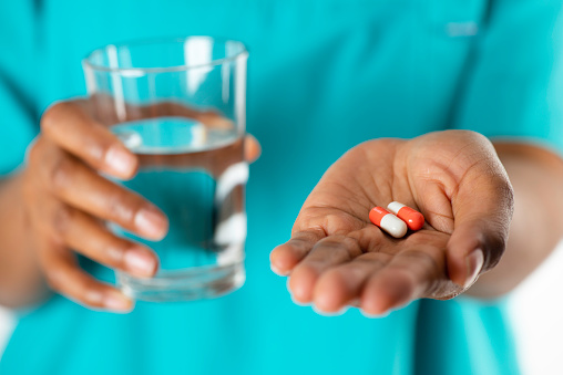 African nurse holding pill, close-up.