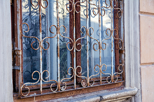The window of an old house behind a metal patterned lattice. Background image of an old house window with peeling paint and rusted bars.