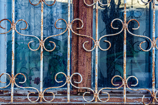 The window of an old house behind a metal patterned lattice. Background image of an old house window with peeling paint and rusted bars.
