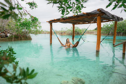 Young Caucasian woman resting in  hammock in water in Bacalar Lagoon in Mexico