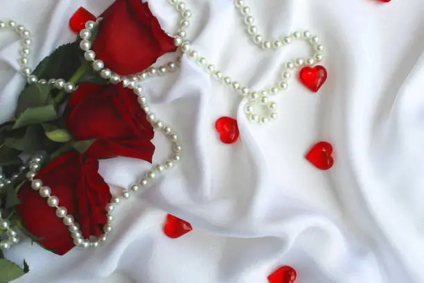 Hearts, roses and a necklace lie on a white draped fabric.