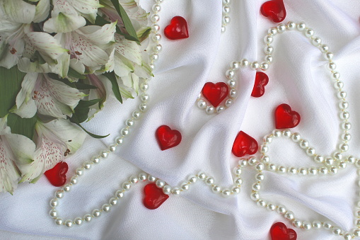 Hearts, flowers and a necklace lie on a white draped fabric.