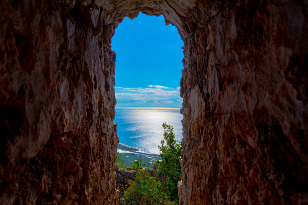 View of the sea through the opening in the ancient stone wall of an ancient building in the ruins of an ancient city. A window in an ancient building overlooking the sea.