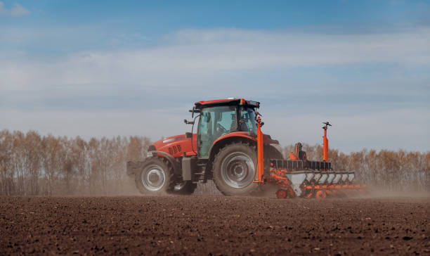 istock Spring sowing season. Farmer with a tractor sows corn seeds on his field. Planting corn with trailed planter. Farming seeding. The concept of agriculture and agricultural machinery. 1393017275