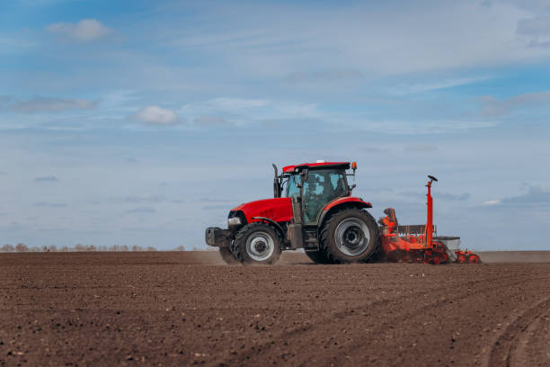 istock Spring sowing season. Farmer with a tractor sows corn seeds on his field. Planting corn with trailed planter. Farming seeding. The concept of agriculture and agricultural machinery. 1393017295