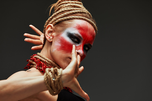 close up portrait of young beautiful girl with colorful face painting. Halloween professional makeup. hair in paint. beauty portrait. neck and hands are wrapped with ropes. Victim Concept.