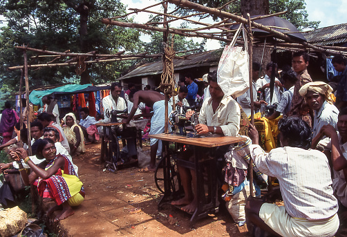 Orissa, Odisha, India - aug 23, 1996:  some tailors, exclusively men, work with their sewing machines for customers who arrive at a weekly market in the hills of Orissa.   Photo from historical archive slide.