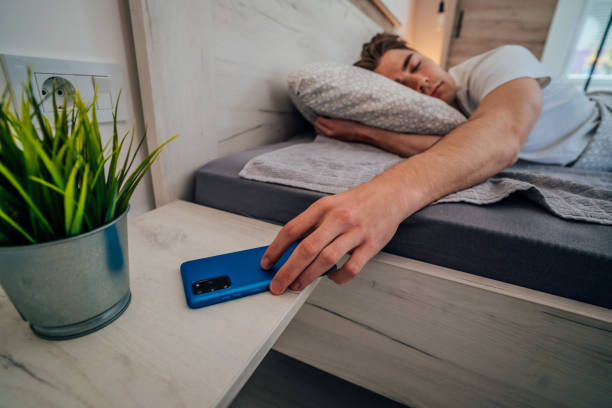 uomo a letto che prende il telefono - dormire troppo foto e immagini stock