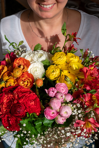 An adult caucasian woman happily holding a bouquet of fresh mixed-colored spring flowers held in her arms. Vertical shot with the concept of happiness, romance, love of nature.