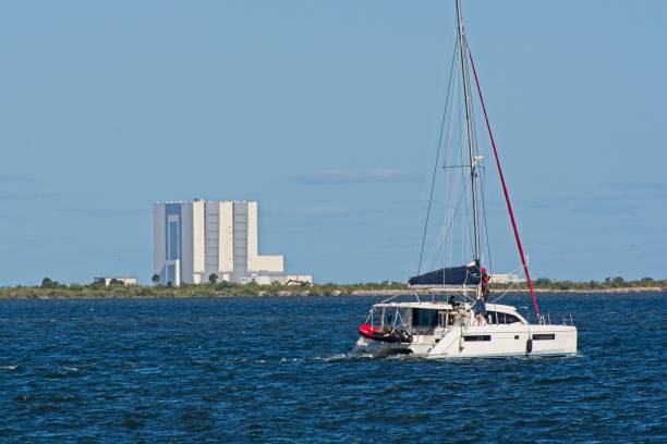 das vehicle assembly building der nasa steht hoch über dem merritt island national wildlife refuge von der anderen seite des indian river mit einem motorisierten katamaran - motoring stock-fotos und bilder