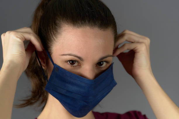 istock nurse in purple uniform looking at camera while putting on surgical mask 1393025201