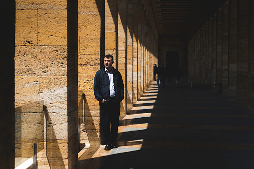 simetri kolonlara sırtını dayamış adam. güneş ışığı fotoğrafın yarısını aydınlatmakta diğer yarısı koyu metin alanı olarak bırakılmıştır.
uzun mimari koridor. full frame makine ile çekilmiştir.