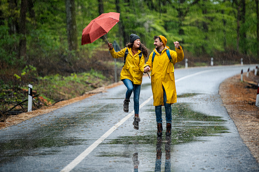 Happy lovely couple in raincoats enjoying raining day in forest