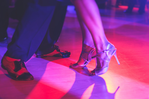 Dancing shoes of a couple, couples dancing traditional latin argentinian dance milonga in the ballroom, tango salsa bachata kizomba lesson, festival on wooden floor, purple, red and violet lights