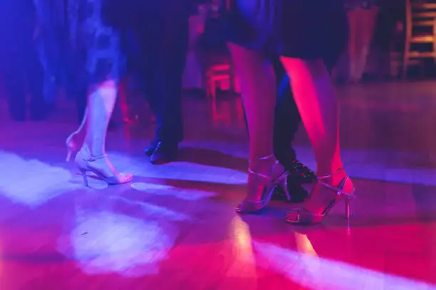 Dancing shoes of a couple, couples dancing traditional latin argentinian dance milonga in the ballroom, tango salsa bachata kizomba lesson, festival on wooden floor, purple, red and violet lights"n
