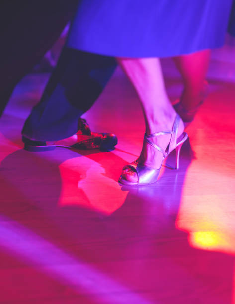 Dancing shoes of a couple, couples dancing traditional latin argentinian dance milonga in the ballroom, tango salsa bachata kizomba lesson, festival on a wooden floor, purple, red and violet lights stock photo