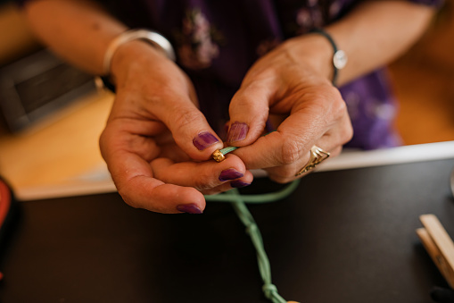 Close up shot of unrecognizable female hands making homemade jewelry. Small business concept.