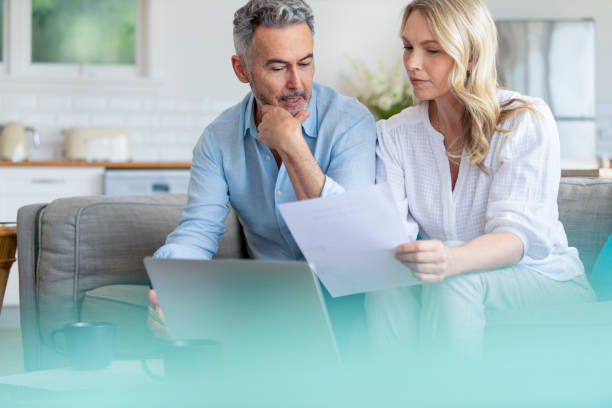 istock Mature couple using a laptop computer and doing paperwork on the sofa 1393034296