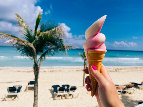 Female hand holding melting ice cream on a sunny hot day  in front of the Cancun beach